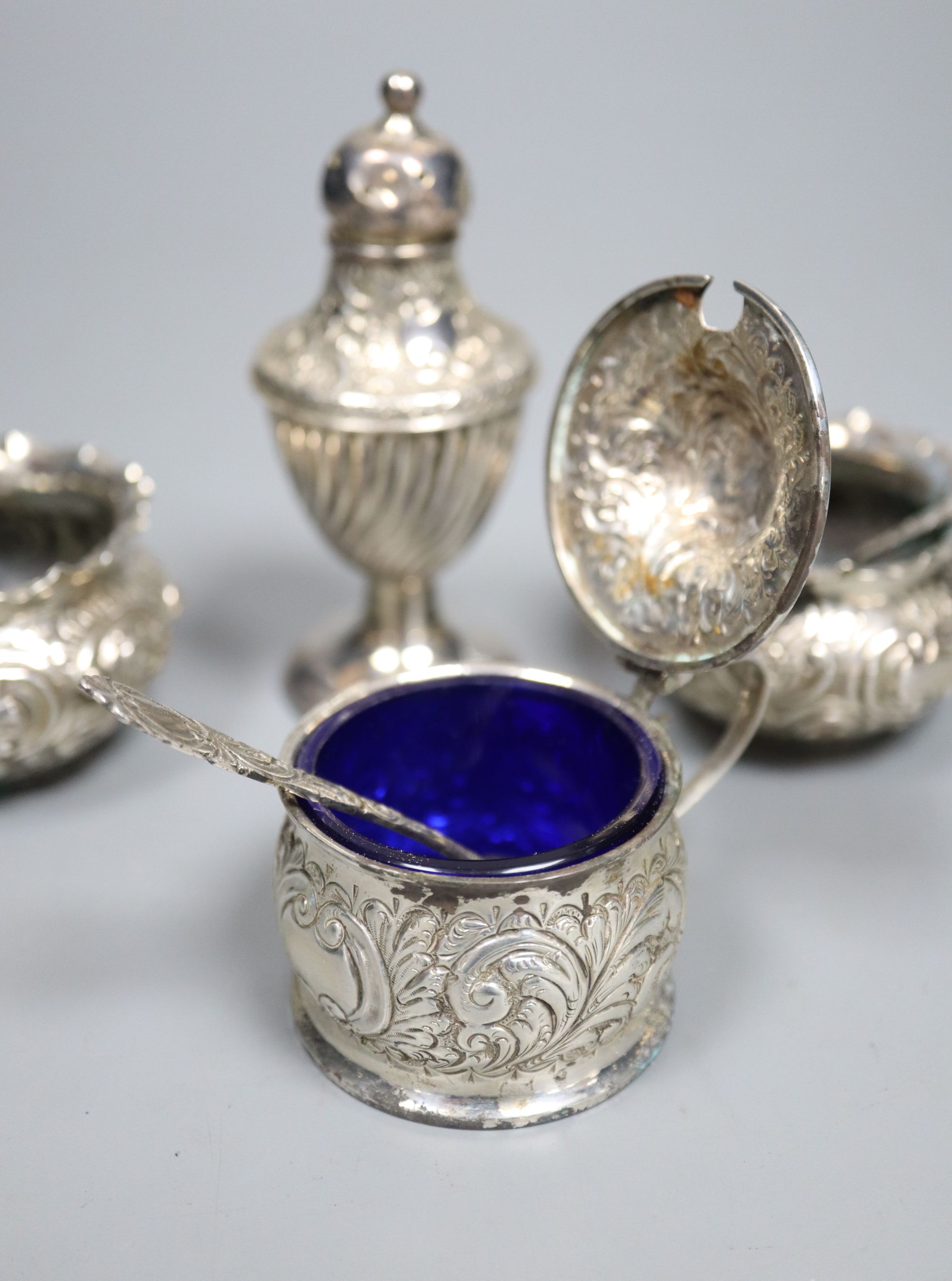 A pair of late Victorian embossed silver salts and one salt spoon, together with a silver mustard pot and a pepper pot (5)